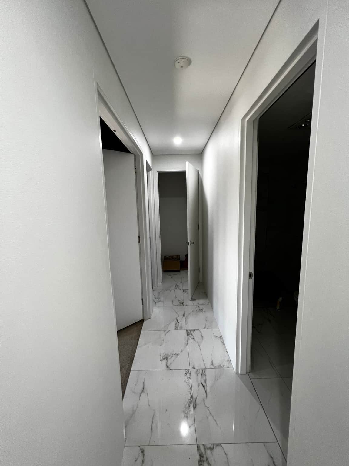 Long white hallway with painted doors, frames and flat ceiling
