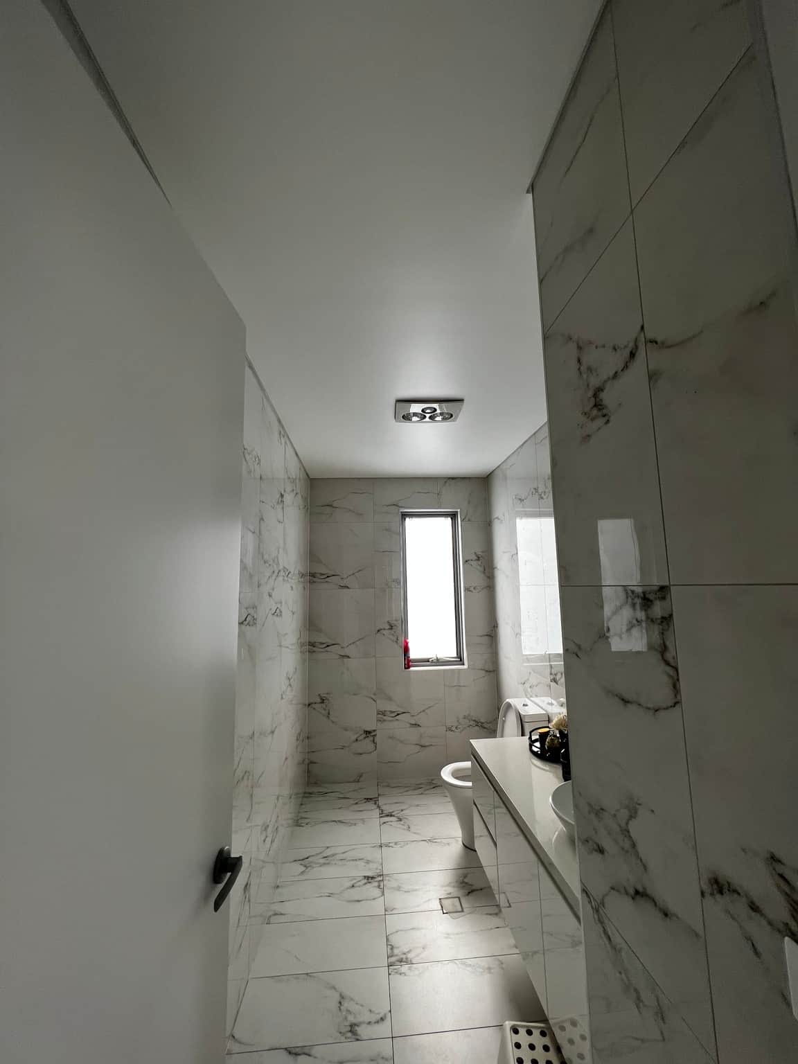 Flat bathroom ceiling above marble-look tiled walls