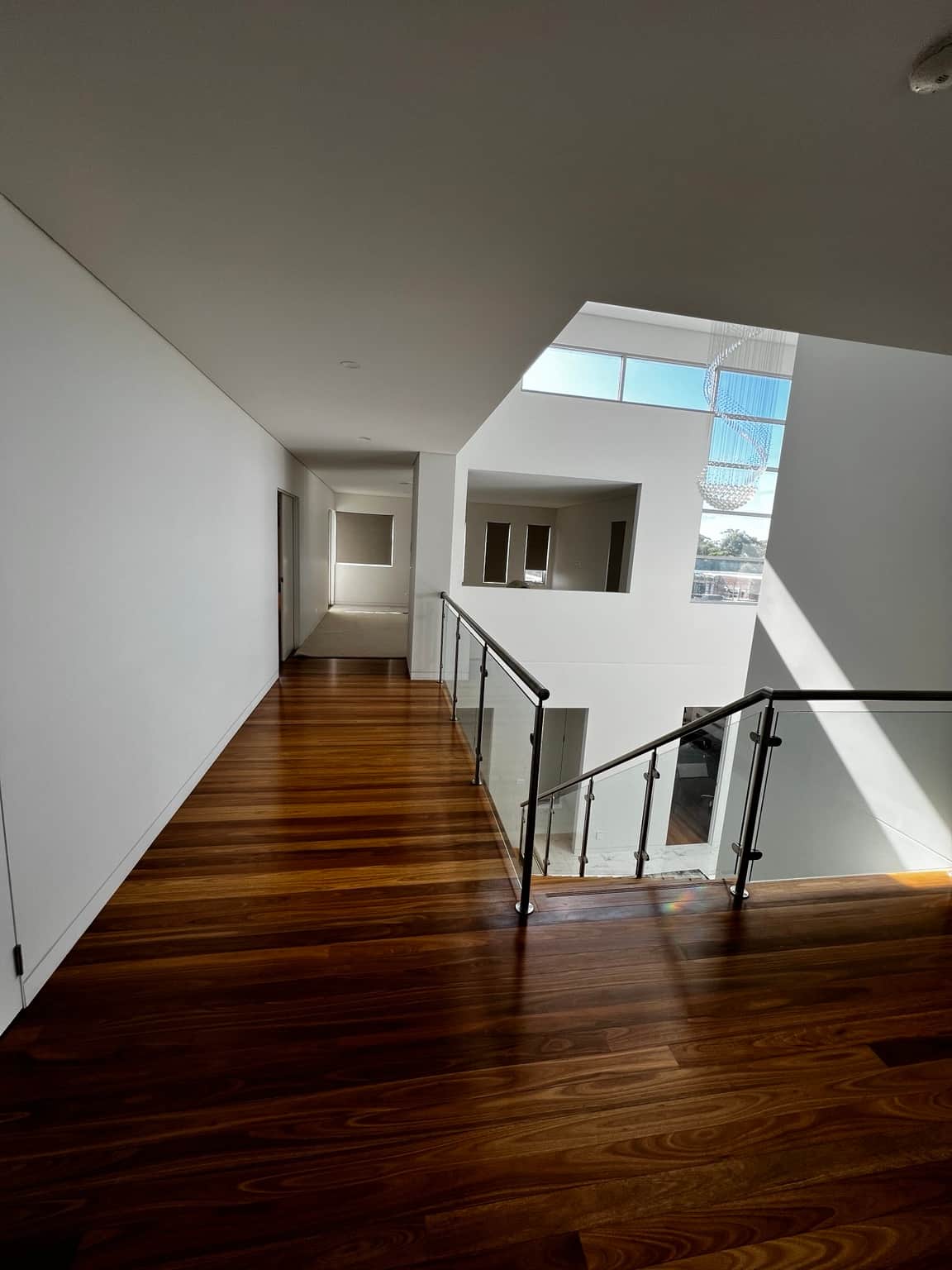 Long upstairs landing with painted walls beside a glass stair balustrade