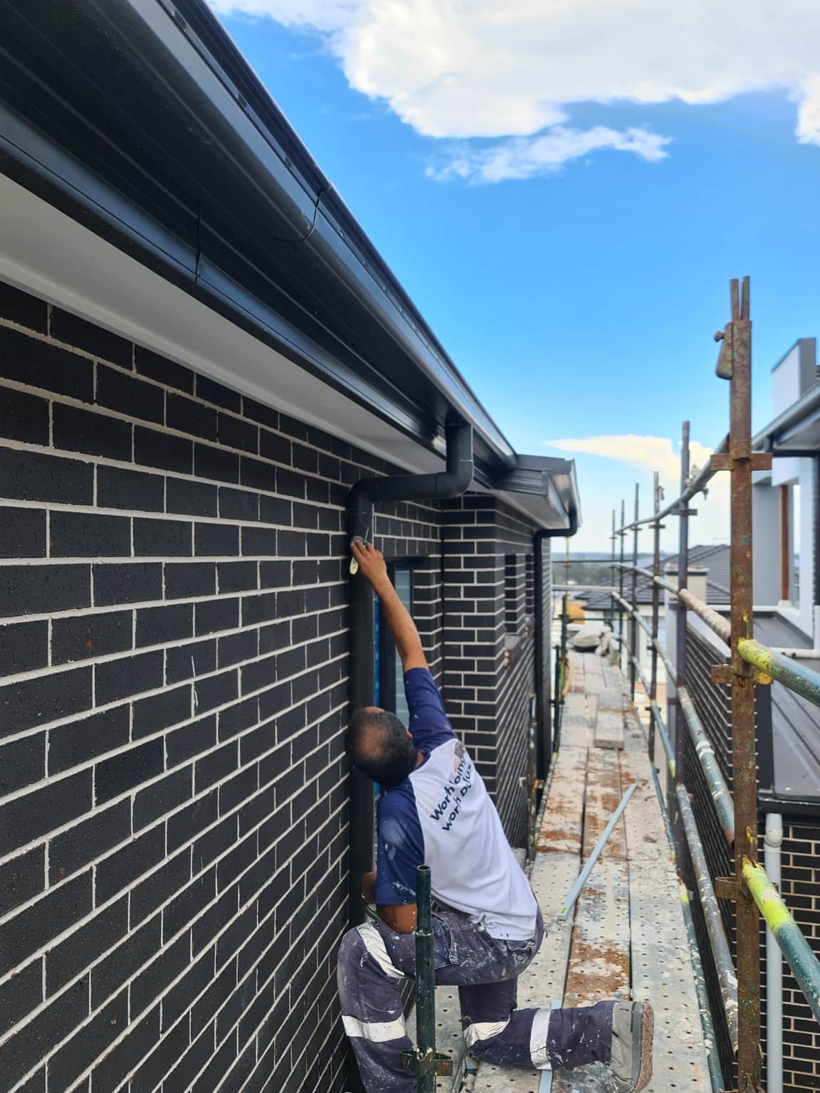 Painter working from scaffolding beside upper-storey brickwork at the Box Hill new build