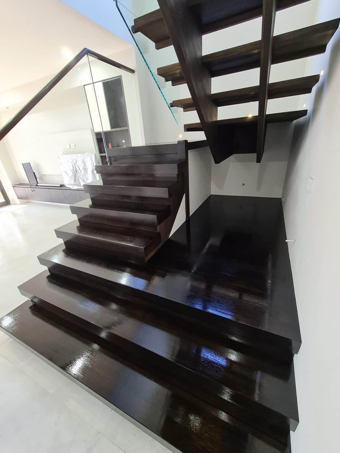 Dark stained timber landing and open-riser staircase beside glass balustrades in a Box Hill home.