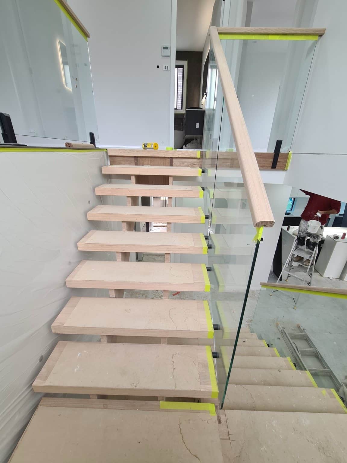 Unfinished open-riser timber stair treads and handrail in Box Hill, with masking tape protecting the glass balustrade.
