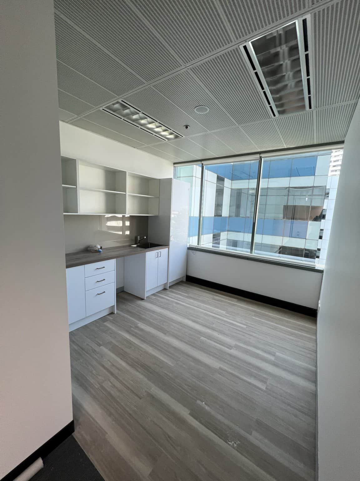 Chatswood office kitchenette with light walls, white cabinetry and large windows.