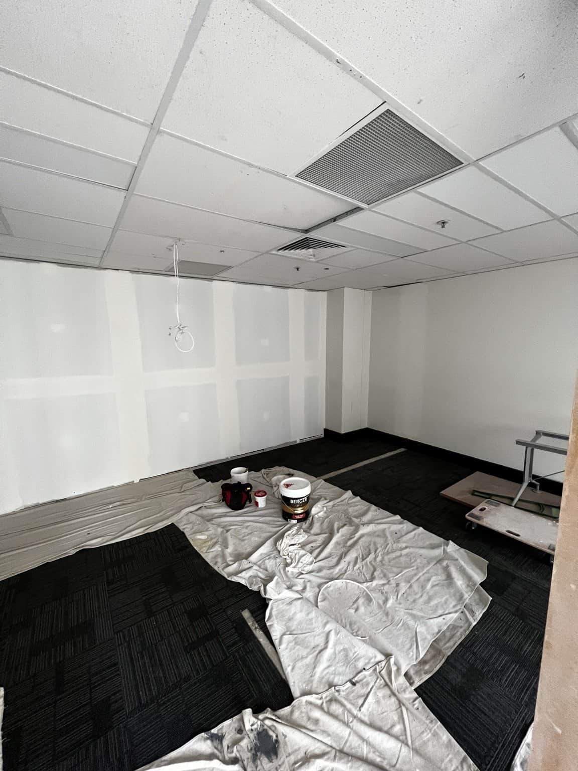Paint containers and protective drop sheets beside a prepared office wall in Chatswood.