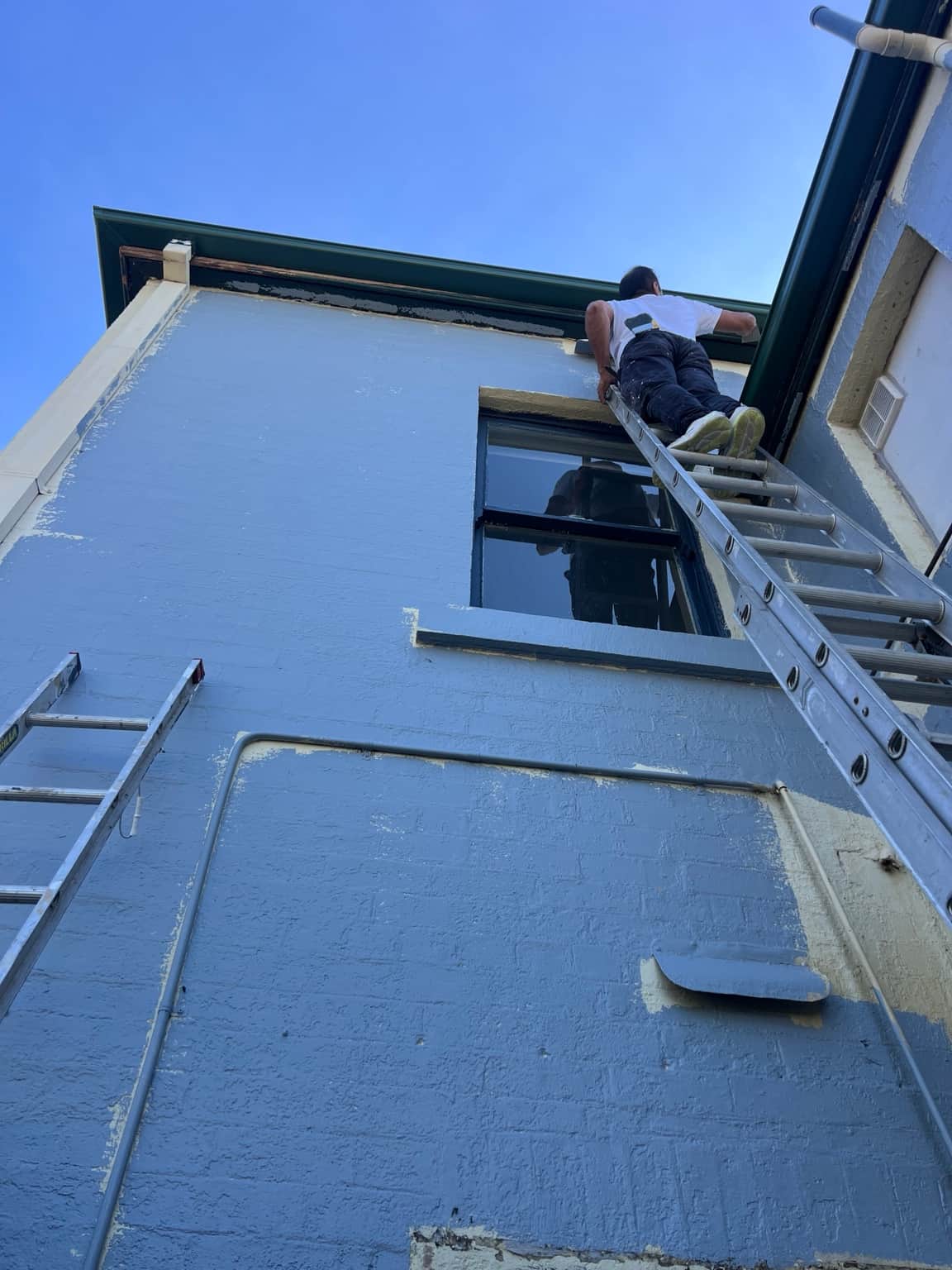 Painter preparing the upper exterior wall from a ladder during the Granville project