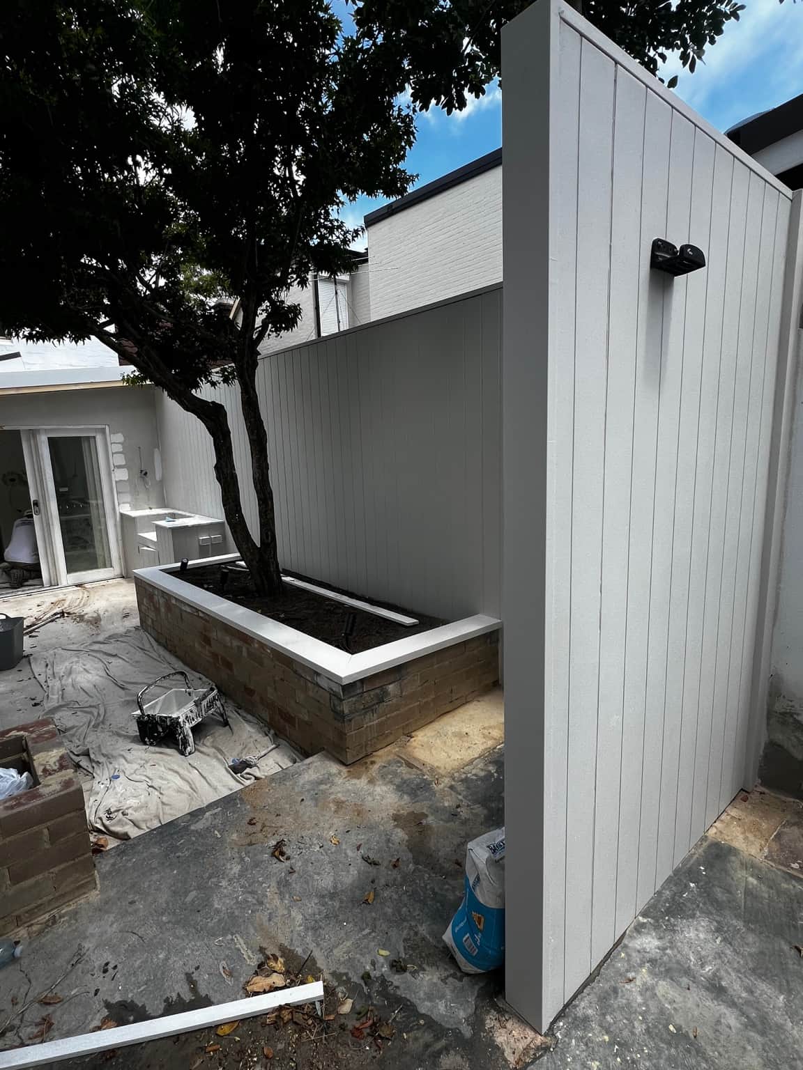Light-coloured courtyard cladding beside an existing tree and raised planter in Newtown