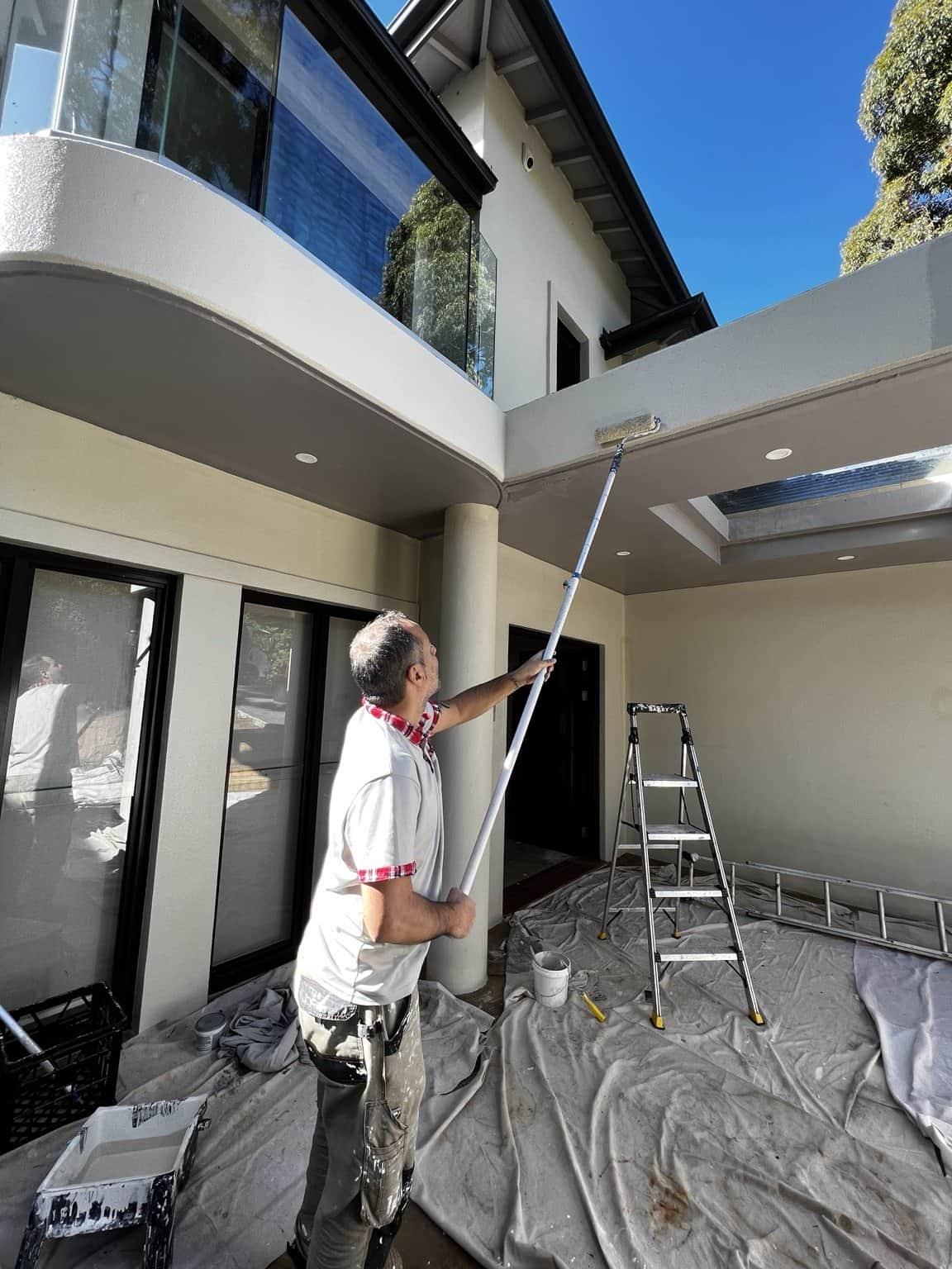 Painter applying paint to an exterior balcony edge in Northbridge, with drop sheets protecting the courtyard.