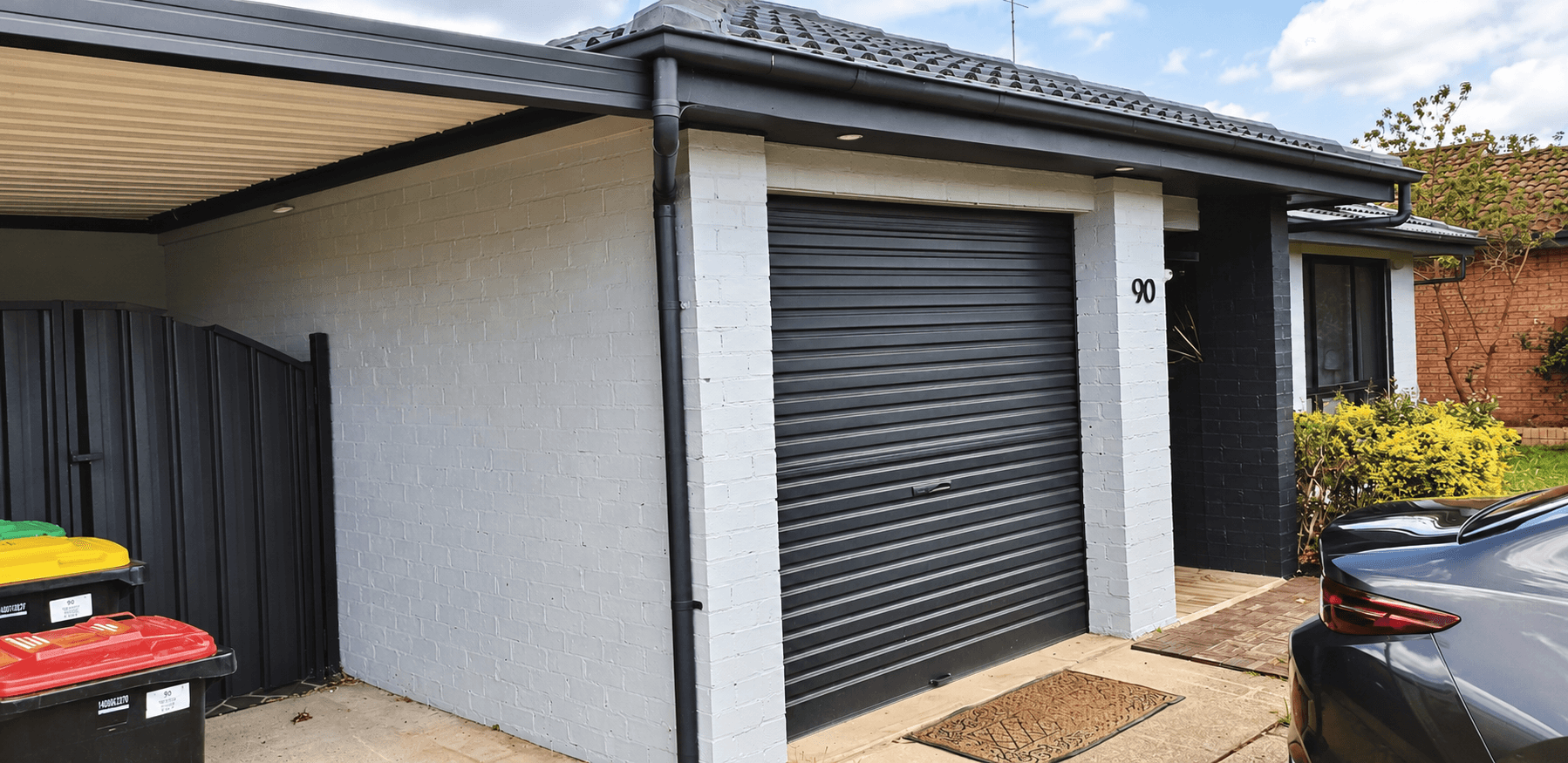 Painted brickwork and charcoal garage door beside the entrance of a St Clair home