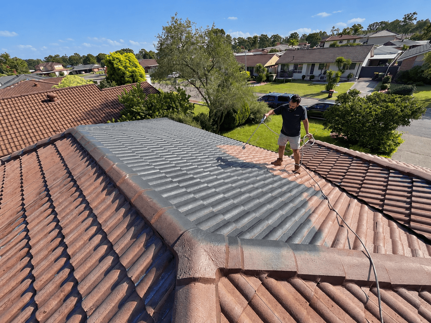 Spray application of roof coating across a tiled roof section in St Clair