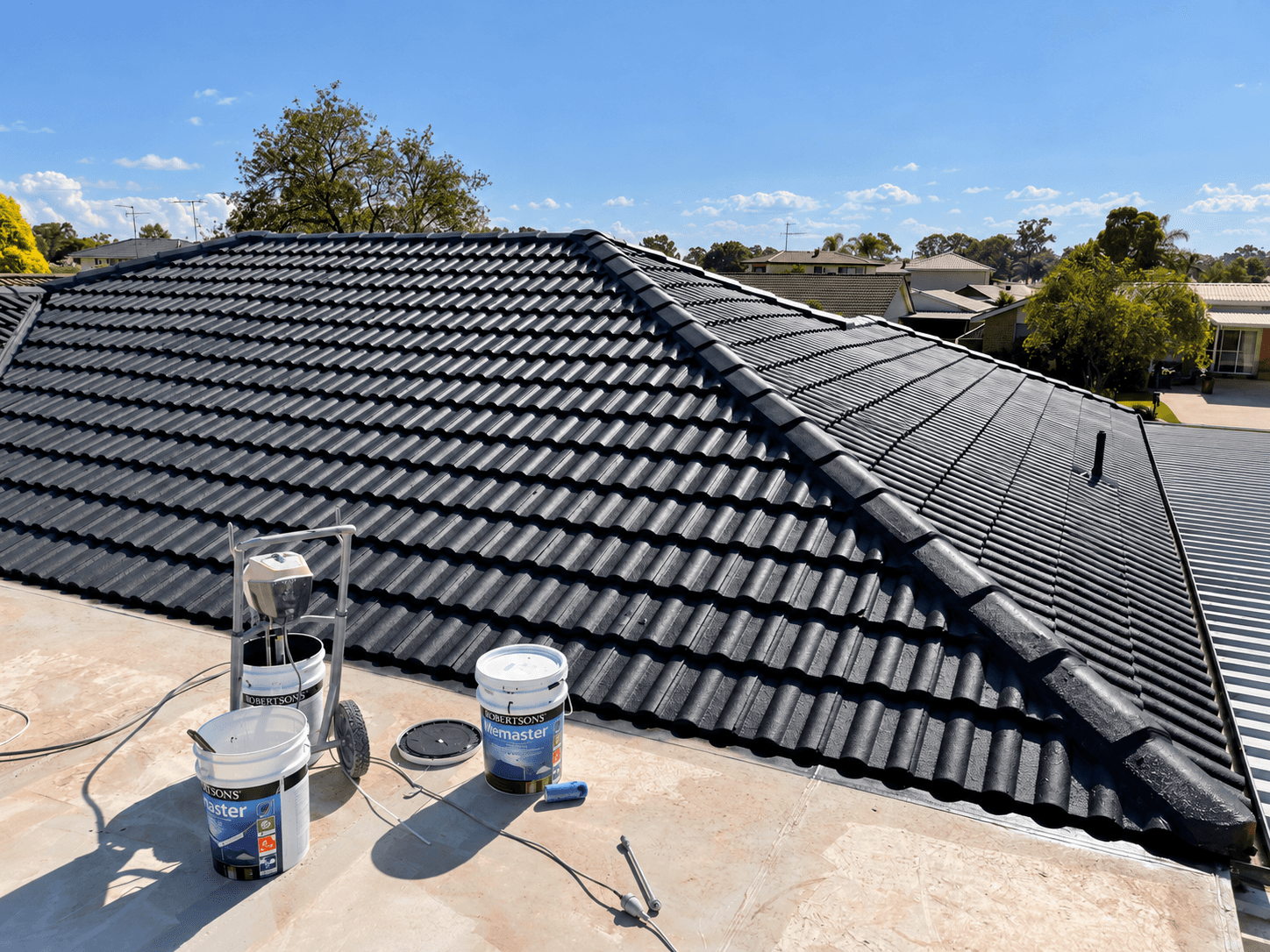 Dark coated roof tiles with Robertson’s coating containers and spray equipment in St Clair