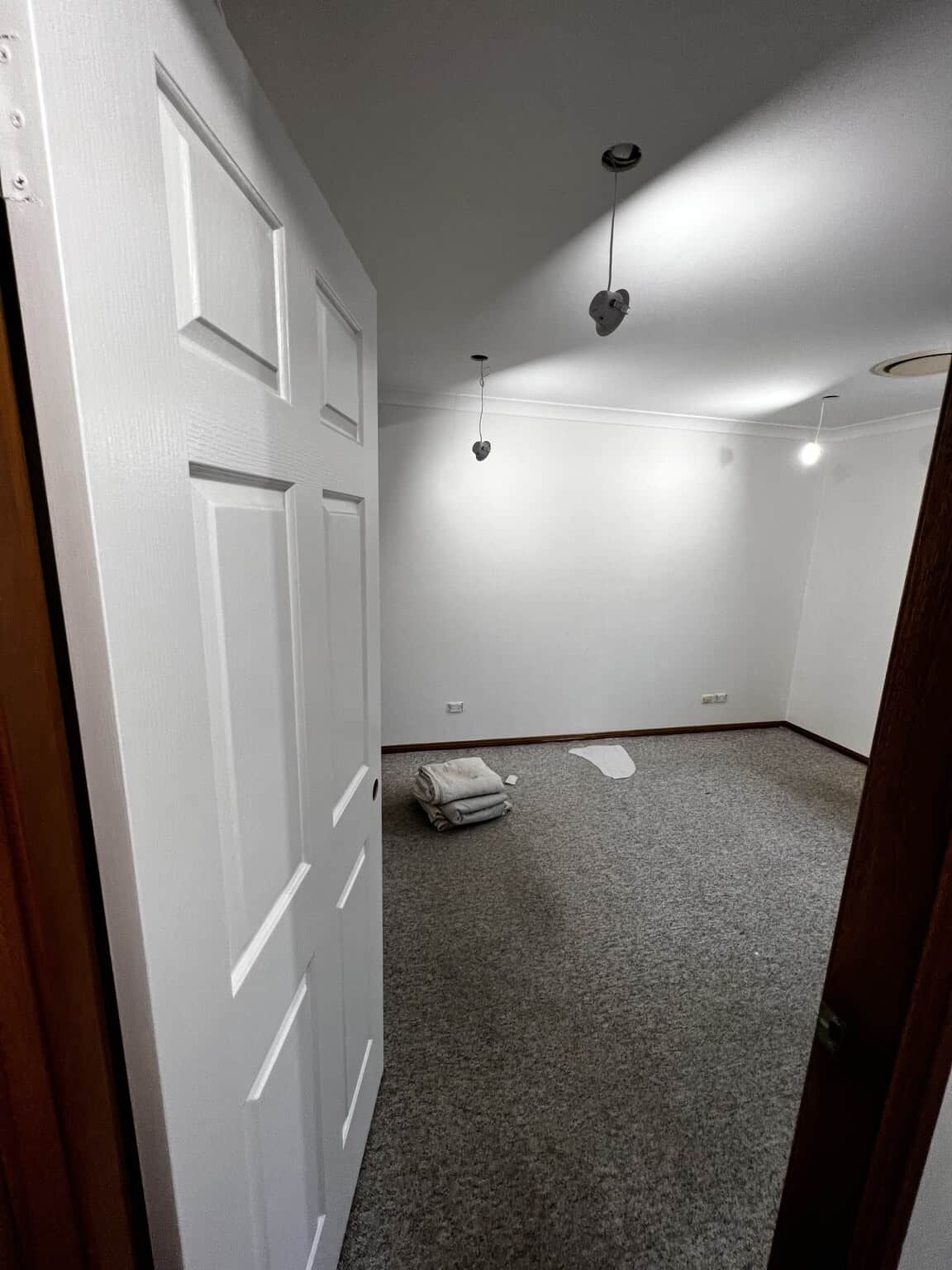 Bedroom viewed through an open painted door, showing finished Natural White walls and a white ceiling.