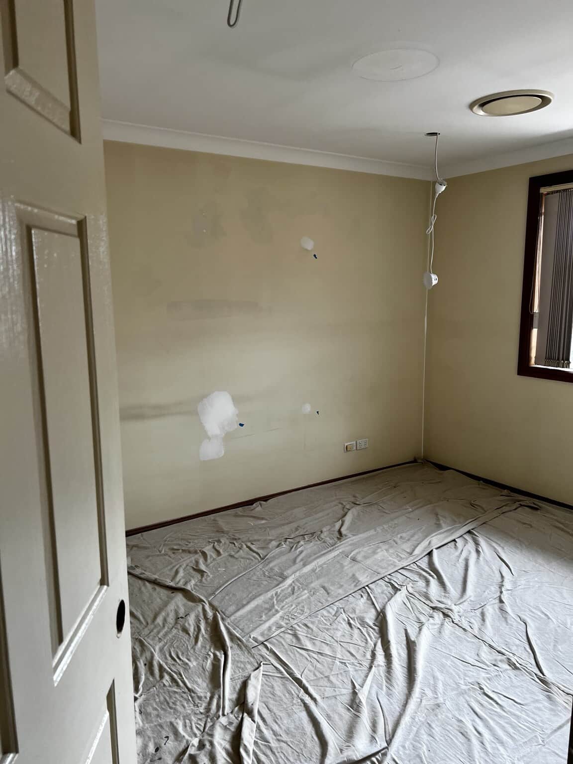 Bedroom wall with visible filler patches and protective drop sheets before painting.