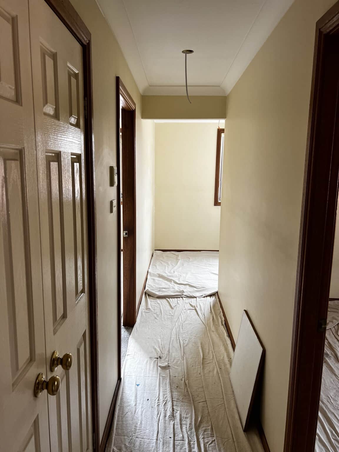 Narrow hallway with beige walls, cream doors and floor protection before painting.