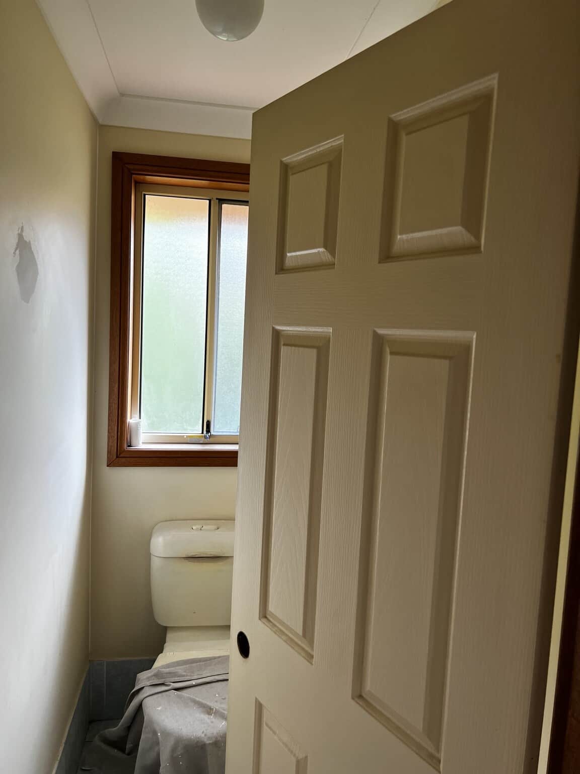 Toilet area with a cream panelled door and visible wall patching before repainting.