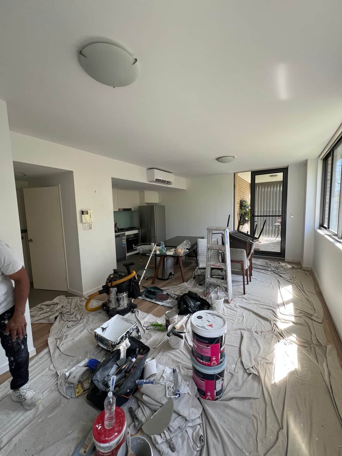 Living and dining area during apartment painting in Wahroonga, with ladders, paint and drop sheets