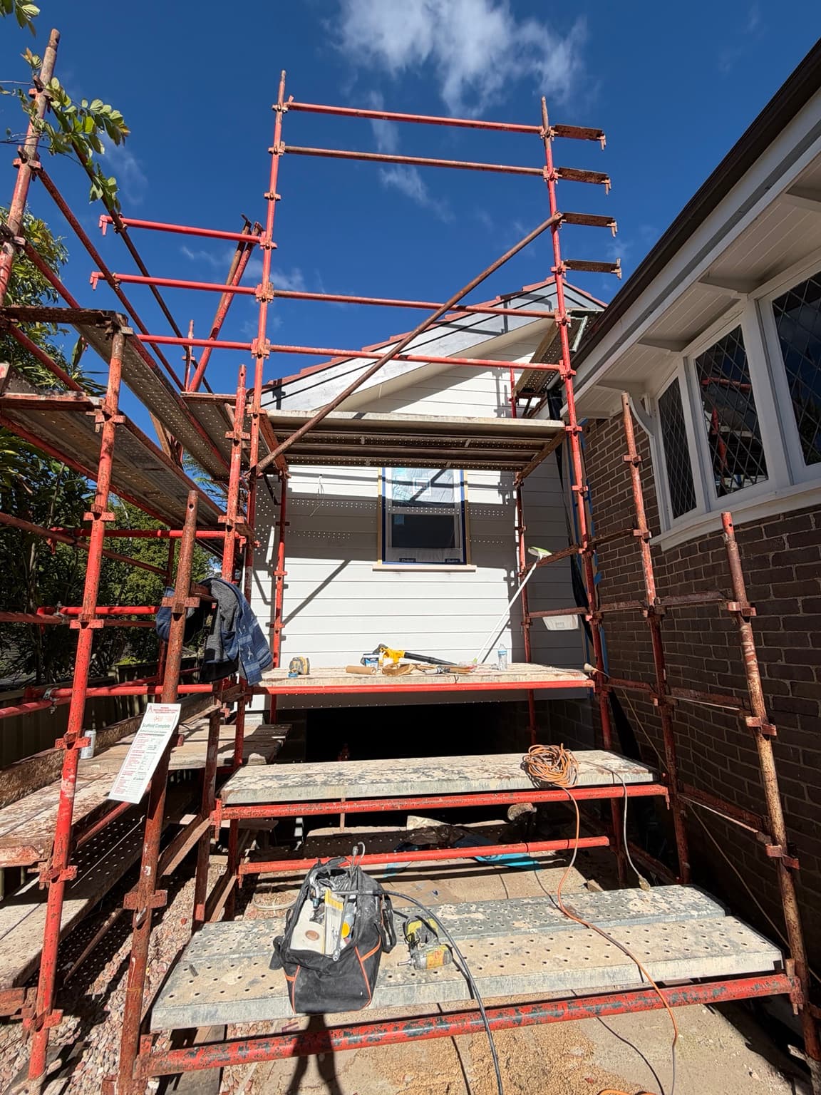 Light painted weatherboard gable with grey fascia and window trim in Beecroft, with scaffolding still in place, before